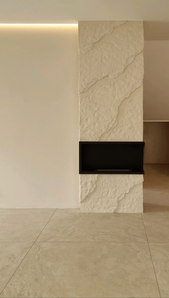 3D bézs sziklafal kivitelezése kandalló köré: gipszkarton szerkezet átalakítása kőhatású modern falburkolattá. Egyedi kézi formálású műszikla design Budapest, Nyíregyháza és Kecskemét, Balaton környékén.